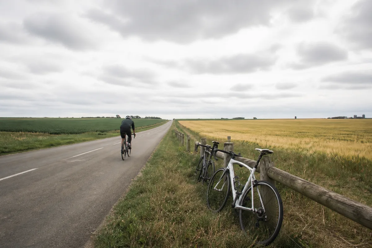 Cycliste roulant seul sur une route de plaine par temps couvert en début de saison